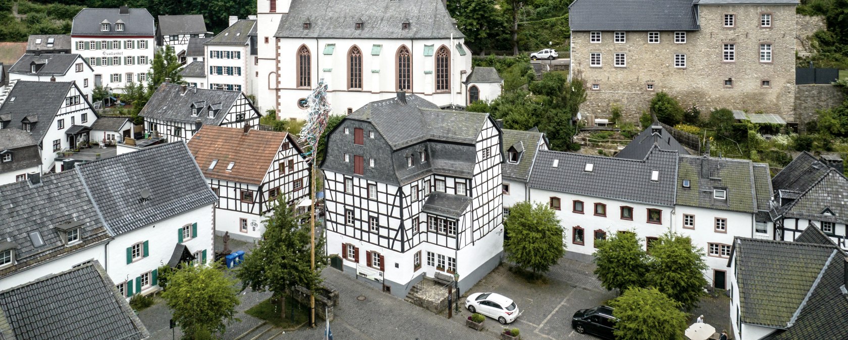 Luftaufnahme von Blankenheim: Fachwerkhäuser, eine Kirche und eine Burg auf einem Hügel, umgeben von grünen Bäumen., © Eifel Tourismus GmbH, Dennis Stratmann Luftaufnahme von Blankenheim: Fachwerkhäuser, eine Kirche und eine Burg auf einem Hügel, umgeben von grünen Bäumen., © Eifel Tourismus GmbH, Dennis Stratmann