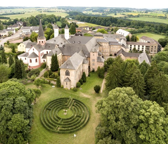Luftaufnahme des Klosters Steinfeld in der Eifel, umgeben von grüner Landschaft und einem Labyrinth im Vordergrund., © Eifel Tourismus, D. Ketz Luftaufnahme des Klosters Steinfeld in der Eifel, umgeben von grüner Landschaft und einem Labyrinth im Vordergrund., © Eifel Tourismus, D. Ketz