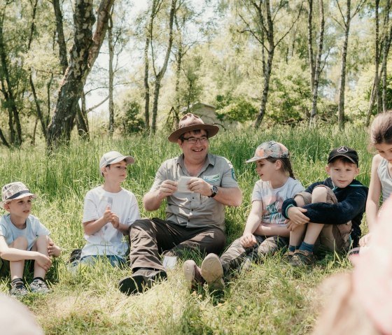 Ranger sitzt mit Kindern im Gras, &copy; A. Kleer