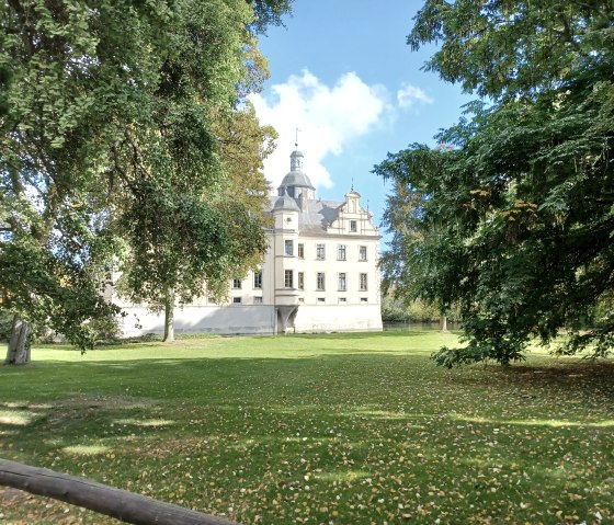 Burg Kriegshoven steht hinter gr&uuml;nen B&auml;umen auf einer gro&szlig;en Rasenfl&auml;che. Der Himmel ist blau mit wenigen Wolken., &copy; Sweco GmbH