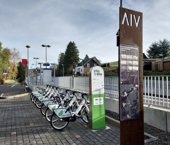 E-Bike-Verleihstation am Bahnhof Dahlem mit mehreren Fahrrädern. Im Hintergrund sind Bäume und ein Gebäude zu sehen., © Sweco GmbH