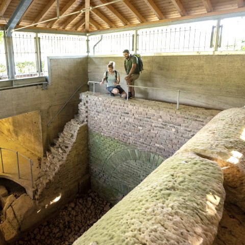 Zwei Personen stehen in einer überdachten römischen Brunnenstube bei Kallmuth und betrachten die antiken Strukturen., © Eifel Tourismus GmbH, Dominik Ketz