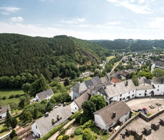 Panoramablick vom Burgturm Reifferscheid auf ein malerisches Dorf mit Kirche, umgeben von gr&uuml;nen H&uuml;geln und W&auml;ldern unter blauem Himmel., &copy; Eifel Tourismus GmbH/D. Ketz