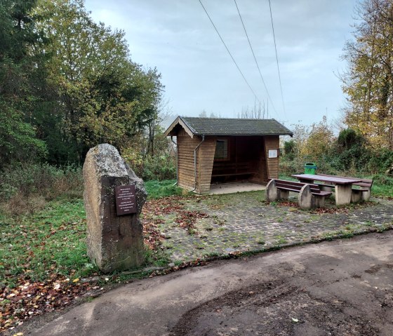 A hiking parking lot with a wooden shelter, picnic table and a large stone. Autumnal trees in the background., &copy; Sweco GmbH