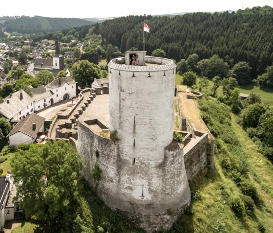 Luftaufnahme der Burg Reifferscheid, umgeben von einem Dorf und W&auml;ldern. Der runde Turm der Burg ist mit einer Fahne beflaggt., &copy; Eifel Tourismus GmbH / D. Ketz