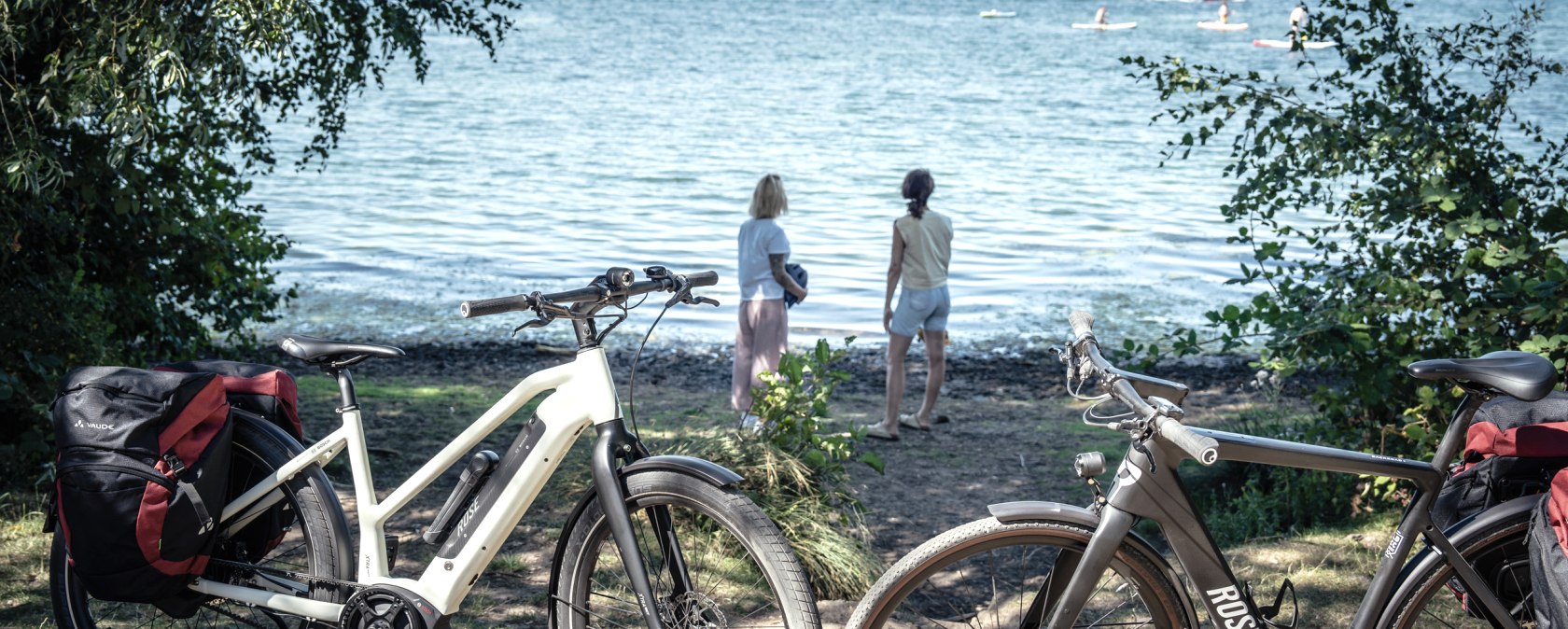 Zwei Fahrr&auml;der stehen am Ufer des Wassersportsees Z&uuml;lpich. Zwei Personen blicken auf das Wasser, wo Segelboote und Surfer zu sehen sind., &copy; Eifel Tourismus GmbH, Dennis Stratmann