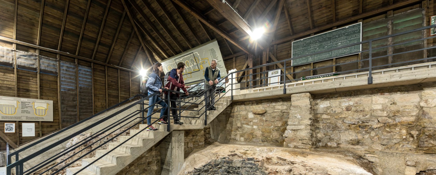 Besucher betrachten eine römische Kalkbrennerei mit steinernen Strukturen und Informationstafeln. Die Anlage ist Teil des UNESCO-Weltkulturerbes., © Eifel Tourismus GmbH AR-shapefruit AG