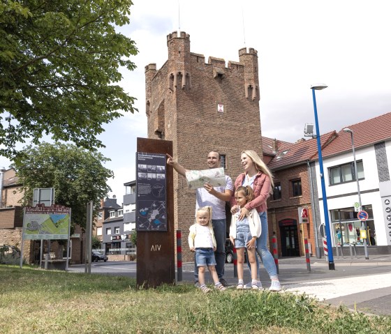 Eine Familie mit zwei Kindern steht vor der Landesburg Z&uuml;lpich, h&auml;lt eine Karte und schaut in die Ferne. Im Hintergrund sind Geb&auml;ude und ein Baum zu sehen., &copy; Eifel Tourismus GmbH, Tobias Vollmer