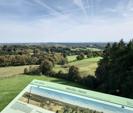 Panoramablick vom Aussichtsturm Weißer Stein über grüne Felder und Wälder, Infotafel im Vordergrund. Windräder am Horizont, blauer Himmel mit Wolken., © Sweco GmbH