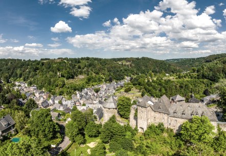 Panoramablick auf Monschau mit der Burg im Vordergrund, umgeben von grüner Landschaft und bewaldeten Hügeln unter blauem Himmel mit Wolken., © Eifel Tourismus GmbH, Dominik Ketz