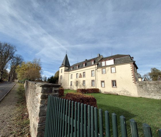 Schloss Schmidtheim mit einem Turm, umgeben von einer Steinmauer und einem gepflegten Garten. Der Himmel ist blau mit leichten Wolken., &copy; Sweco GmbH