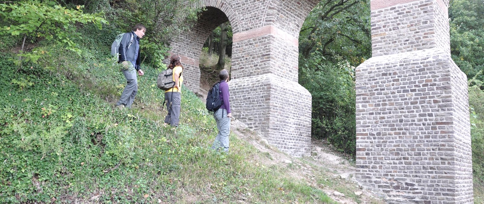 Drei Wanderer erkunden die Aquäduktbrücke Vussem auf dem Römerkanal-Wanderweg, umgeben von üppigem Grün., © Wandermagazin/ N. Glatter
