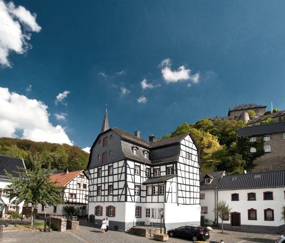 Fachwerkh&auml;user in Blankenheim, umgeben von gr&uuml;nen H&uuml;geln und blauem Himmel. Eine Burg thront im Hintergrund auf einem H&uuml;gel., &copy; Eifel Tourismus GmbH, D. Ketz