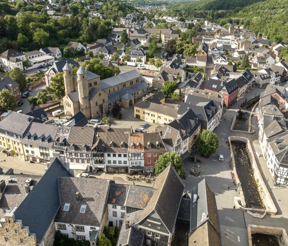 Luftaufnahme von Bad Münstereifel zeigt historische Gebäude, eine Kirche und einen Flusslauf, umgeben von grünen Hügeln und Bäumen., © Eifel Tourismus GmbH, Dominik Ketz