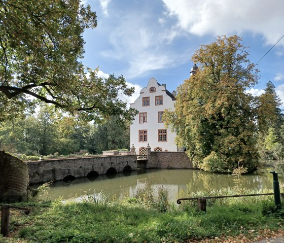 Die Wasserburg Metternich mit einer Steinbr&uuml;cke, umgeben von B&auml;umen und einem Wassergraben, unter blauem Himmel im Herbst., &copy; Nordeifel Tourismus GmbH