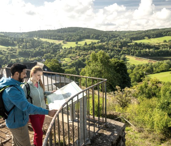 Zwei Personen stehen auf einer Aussichtsplattform und betrachten eine Karte. Im Hintergrund ist eine gr&uuml;ne, h&uuml;gelige Landschaft zu sehen., &copy; Eifel Tourismus, Dominik Ketz